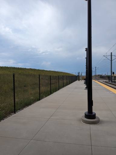 A tram platform in the middle of nowhere, with grassy hills around it, and a lamp pole in the center of the frame.